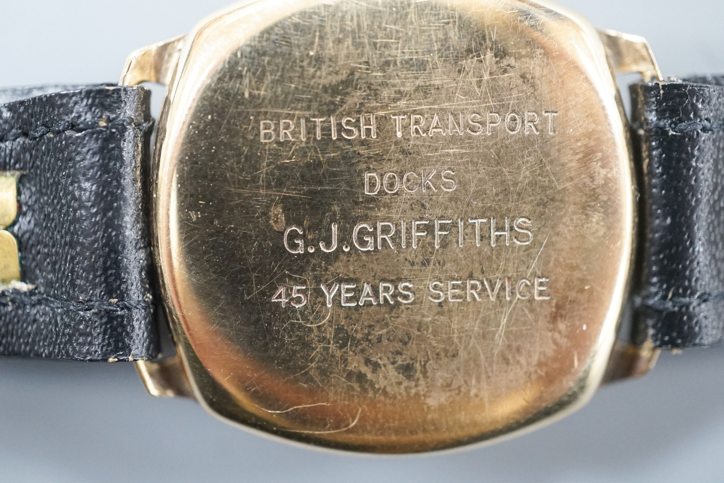 A gentleman's 9ct. gold wristwatch by Garrard in cushion case, silvered dial, baton and Roman numerals, Swiss 16 jewel movement, c.1957 inscription to back, black leather strap, cased diameter, 30mm, gross 24 grams.